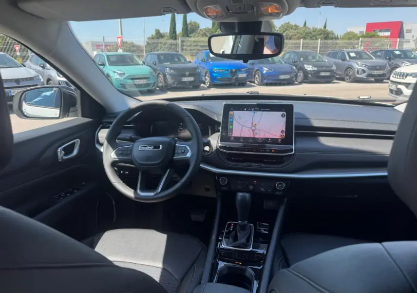 Vue intérieure avant du Jeep Compass 2025 avec tableau de bord noir, écran tactile central et volant multifonction.
