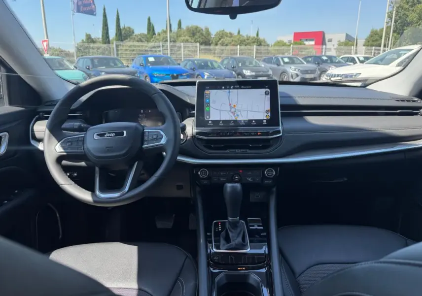 Vue intérieure avant du Jeep Compass 2025 blanc, montrant le volant, écran tactile central et levier de vitesses automatique.