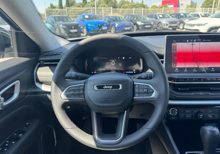 Vue intérieure centrée sur le volant Jeep d'un Compass 2025 avec tableau de bord numérique et écran tactile large.