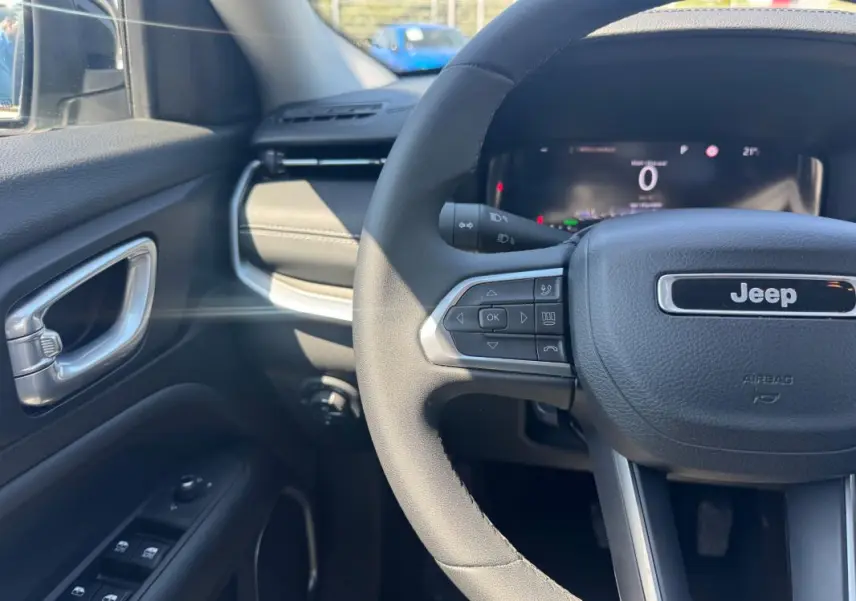 Vue intérieure côté conducteur du Jeep Compass blanc 2025, volant multifonctions et tableau de bord numérique visibles.