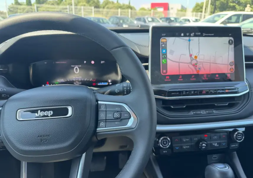 Vue intérieure centrée sur le volant Jeep noir et l'écran tactile affichant un GPS dans un Compass blanc 2025.