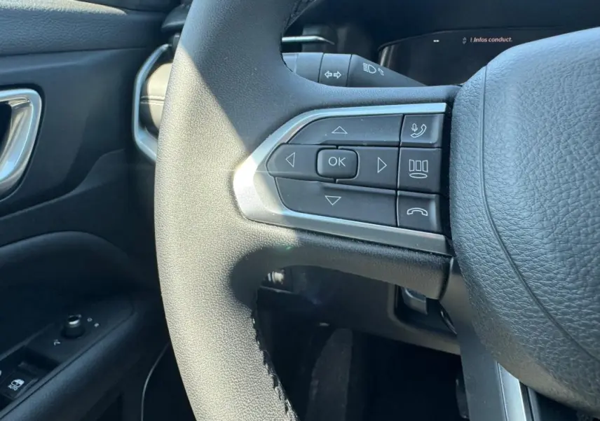 Gros plan sur les commandes à gauche du volant noir du Jeep Compass blanc, avec bouton OK et commandes vocales.