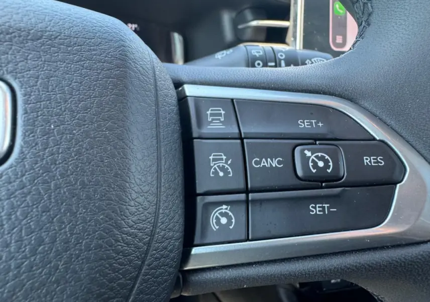 Gros plan sur les commandes du régulateur de vitesse au volant noir du Jeep Compass blanc 2025.