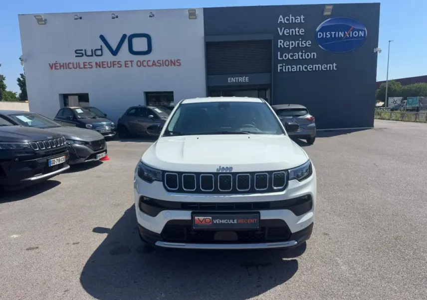 Vue avant d'un Jeep Compass blanc 2025 garé devant un concessionnaire avec calandre distinctive à sept fentes.
