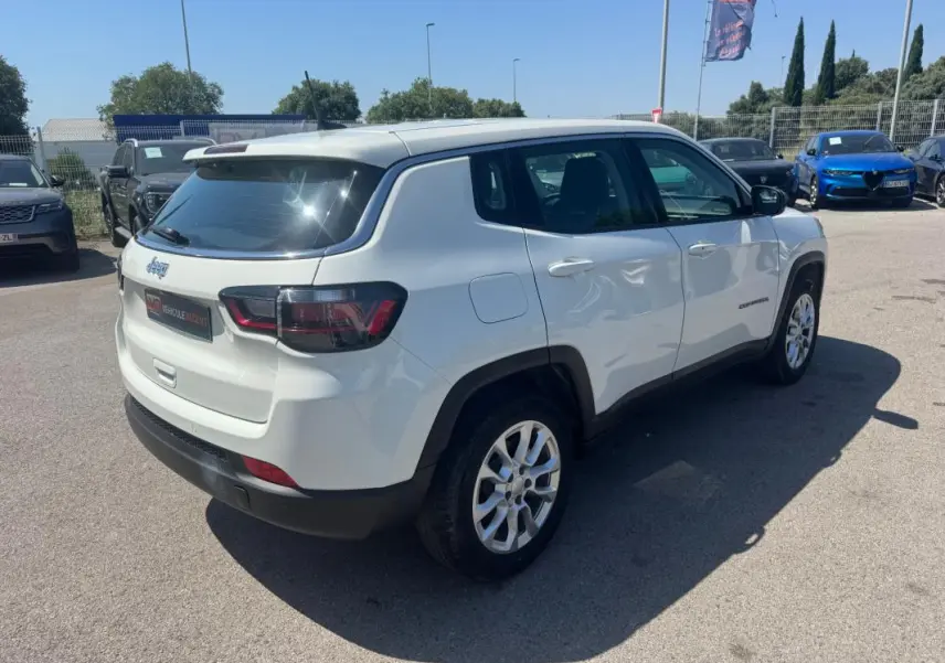 Jeep Compass blanc en vue 3/4 arrière droit, avec jantes alliage et vitres teintées, stationné en extérieur.
