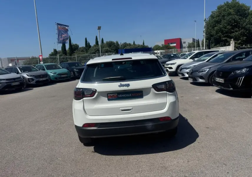 Vue arrière d'un Jeep Compass blanc 2025 garé en extérieur, avec feux arrière sombres et logo Jeep visible.