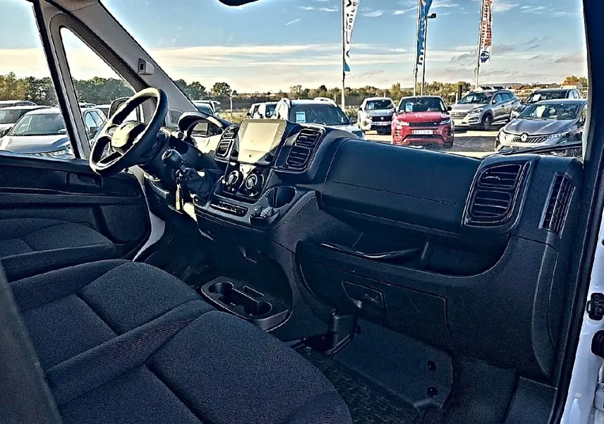 Vue intérieure côté conducteur du Peugeot Boxer Fourgon blanc, mettant en valeur le tableau de bord et la banquette avant noire.