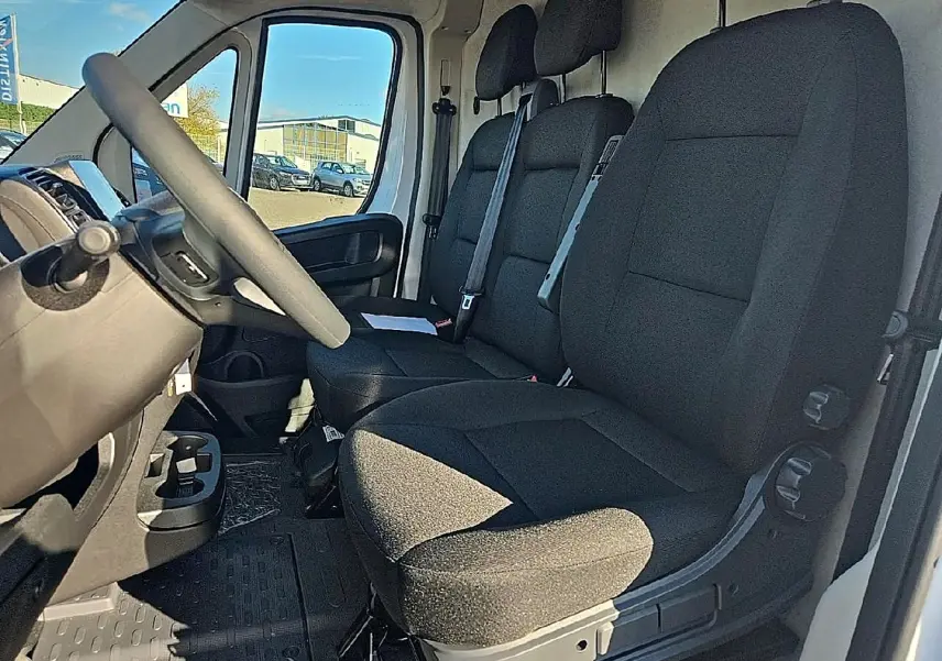 Vue intérieure côté conducteur du Peugeot Boxer Fourgon blanc, montrant la banquette avant noire et le volant.