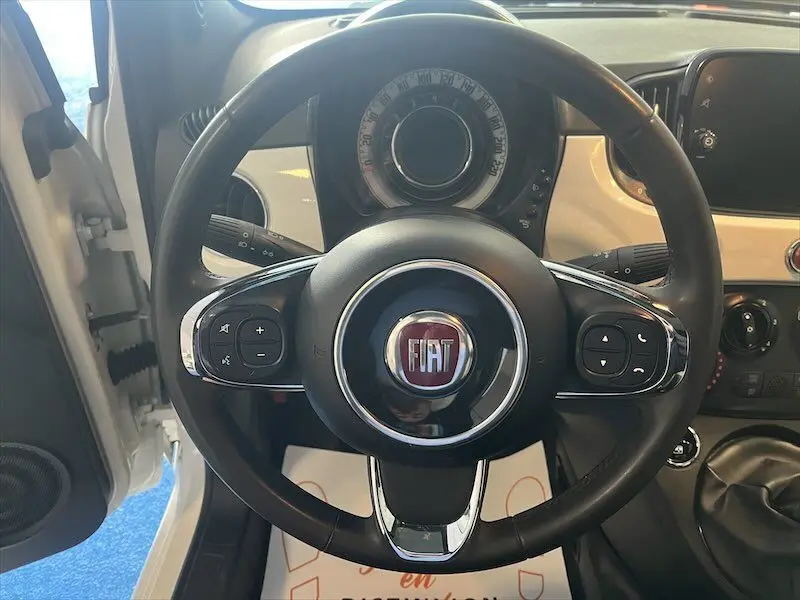 Vue intérieure centrée sur le volant noir de la Fiat 500 blanche, avec tableau de bord et commandes visibles.