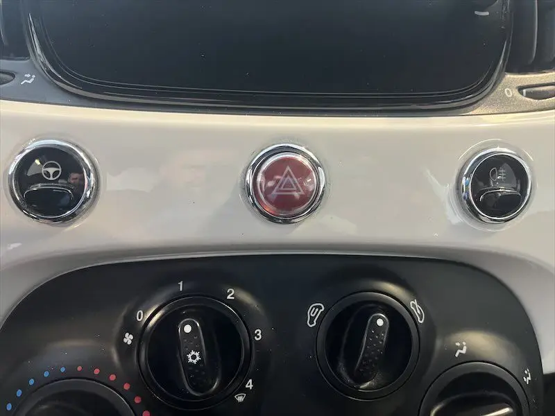 Gros plan sur la console centrale blanche de la Fiat 500 2021, mettant en valeur les boutons de commande et le bouton d'alerte rouge.