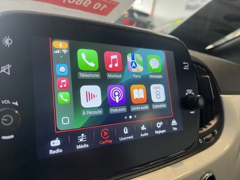 Écran tactile central de la Fiat 500 blanche de 2021 affichant l'interface Apple CarPlay avec plusieurs applications colorées.