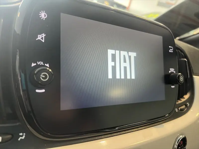 Écran tactile central affichant le logo FIAT dans l'habitacle clair d'une Fiat 500 blanche, vue rapprochée.