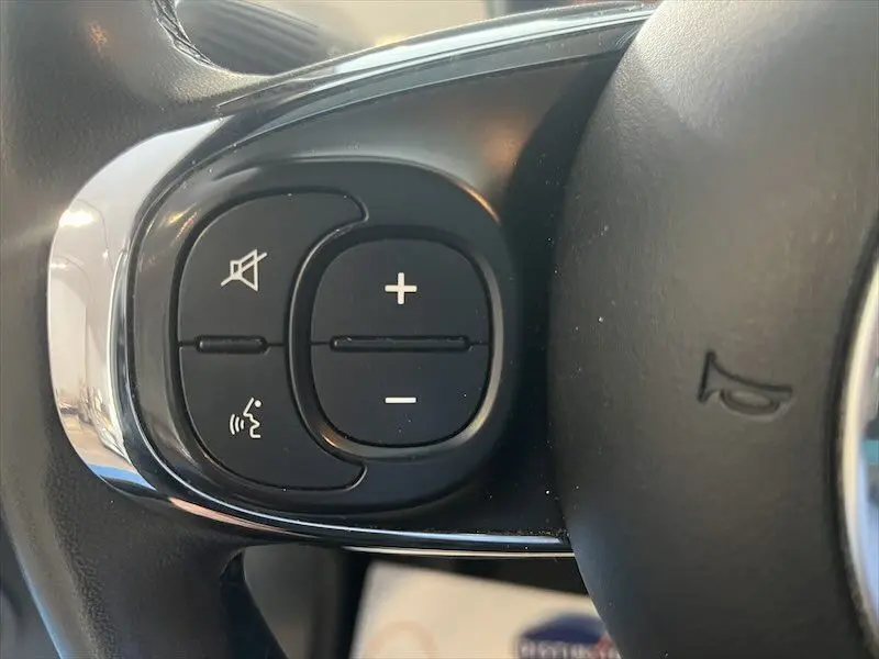 Gros plan sur les commandes de volume et de sourdine sur le volant noir de la Fiat 500 blanche de 2021.