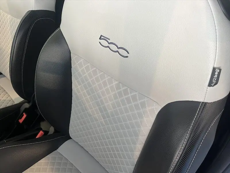 Gros plan sur la sellerie bicolore noire et blanche avec logo 500 brodé sur le siège avant d'une Fiat 500 blanche.