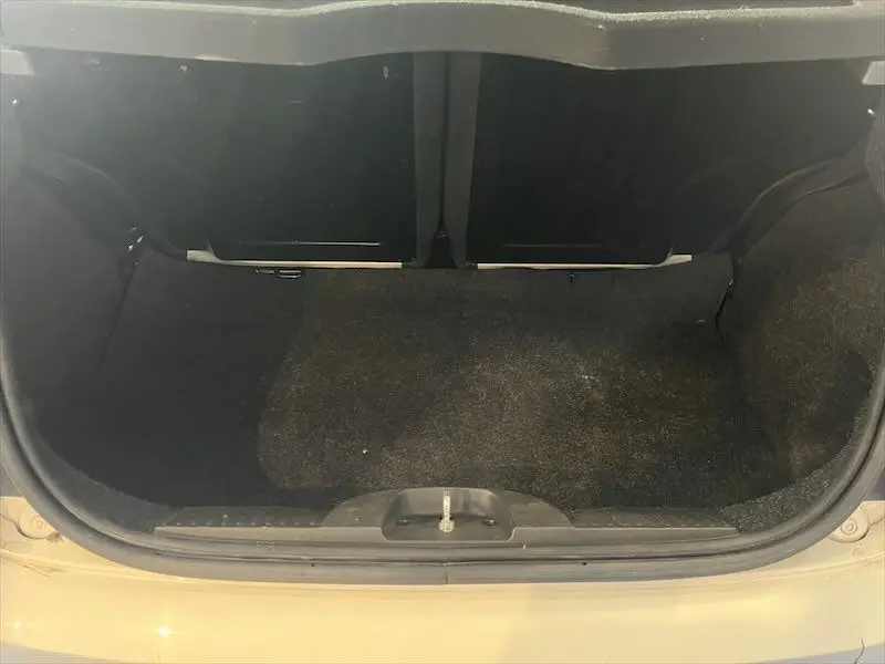 Coffre ouvert vu de face d'une Fiat 500 blanche, montrant l'espace de chargement vide et la moquette noire.