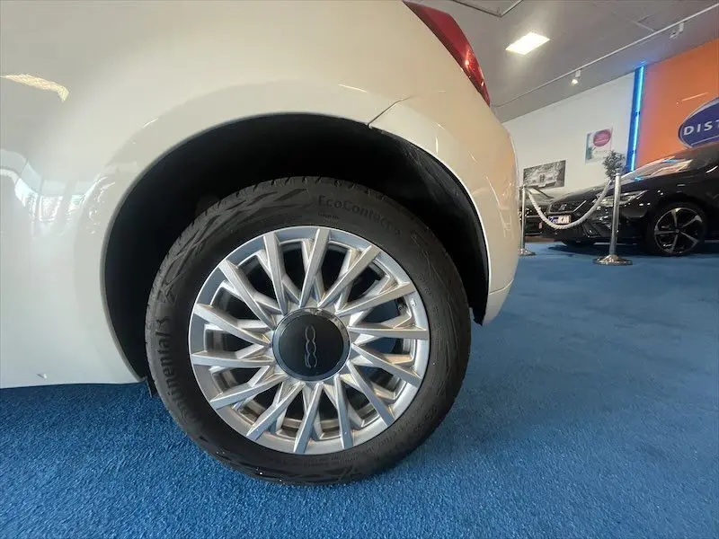 Gros plan sur la roue arrière droite d'une FIAT 500 blanche, avec jante argentée au design étoilé, en intérieur showroom.