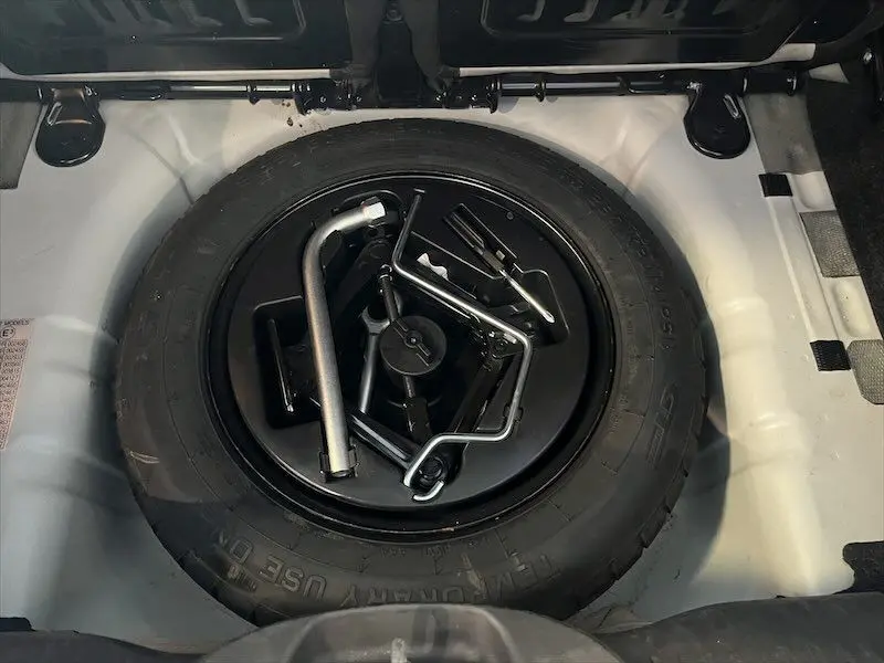 Gros plan sur la roue de secours et les outils de la FIAT 500 blanche, visibles dans le coffre ouvert.