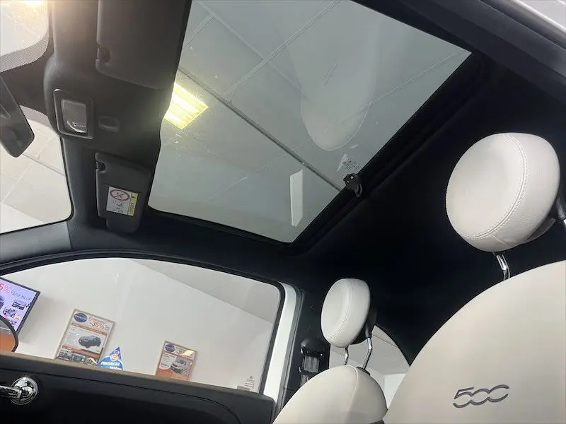 Vue intérieure du toit panoramique et des sièges blancs de la Fiat 500 DolceVita 2021 avec logo brodé sur l'appui-tête.