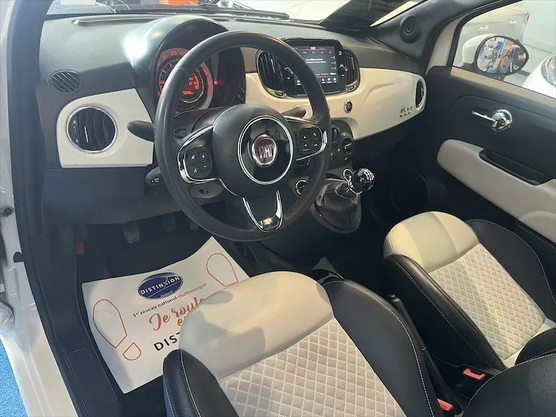 Intérieur de la Fiat 500 blanche vue côté conducteur, tableau de bord et sièges bicolores noir et blanc élégants.