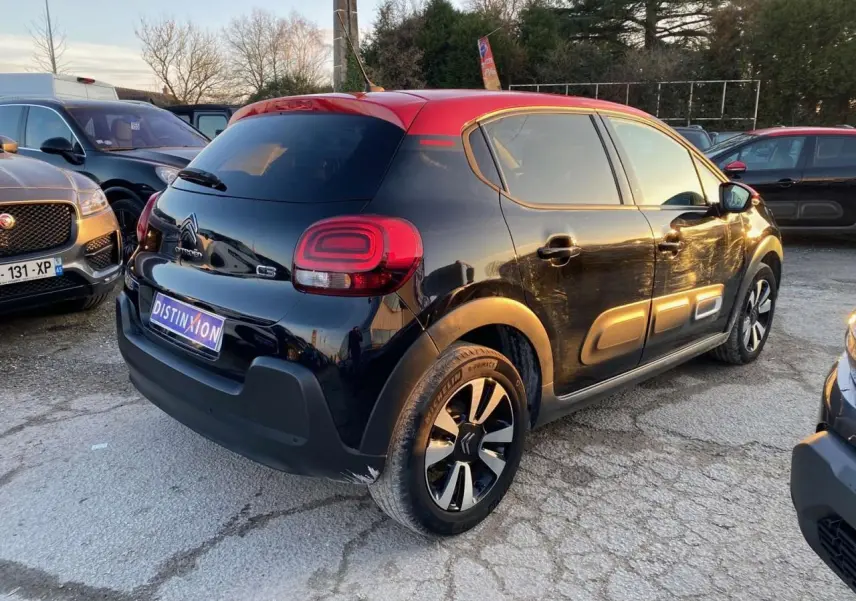 Vue 3/4 arrière droite d'une Citroën C3 Shine 2023 noire avec toit rouge et jantes alliage diamantées.