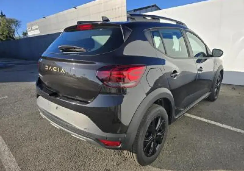 Vue 3/4 arrière droite d'une Dacia Sandero Stepway 2025 noir nacré avec jantes noires et barres de toit.