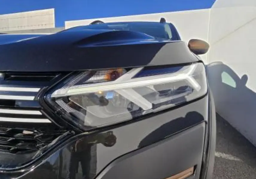 Gros plan sur le phare avant droit et la calandre noire nacrée du Dacia Sandero III Stepway avec détails chromés.