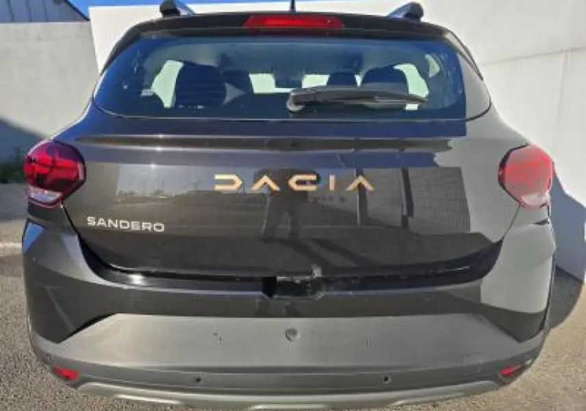 Vue arrière d'une Dacia Sandero III Stepway noire nacrée avec logo doré et feux rouges visibles.