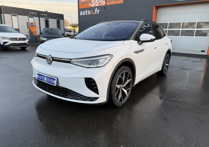 Volkswagen ID.4 GTX blanc glacier en 3/4 avant droit avec toit noir et jantes bi-colores sur parking humide.