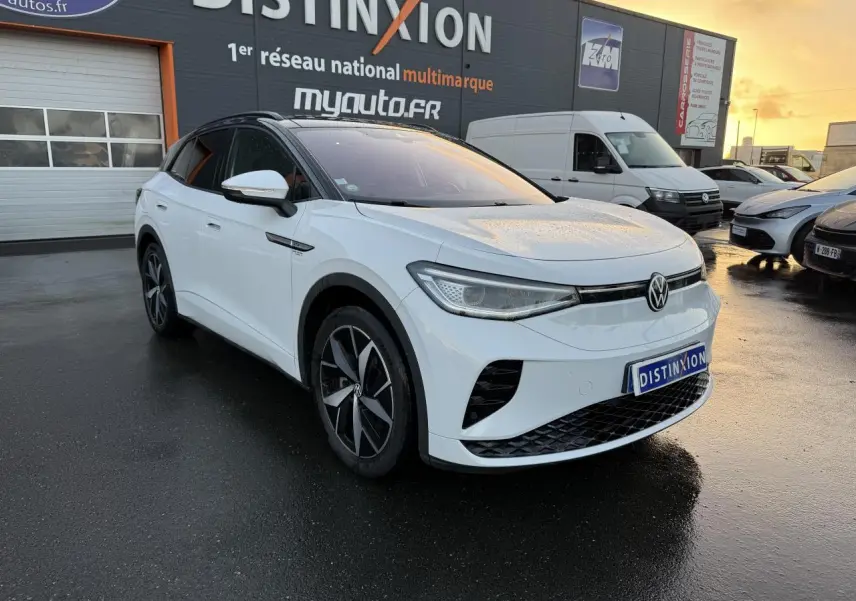 Volkswagen ID.4 GTX blanc glacier en 3/4 avant droit, toit noir et jantes bi-colores, stationné devant un garage