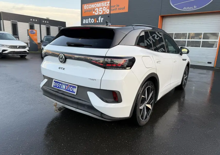 Vue 3/4 arrière droite d'un Volkswagen ID.4 GTX blanc glacier métallisé avec toit noir et crochet d'attelage.