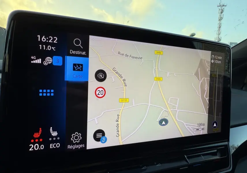 Vue intérieure du tableau de bord du Volkswagen ID.4 GTX blanc, écran tactile affichant la navigation et la température à 20°C.