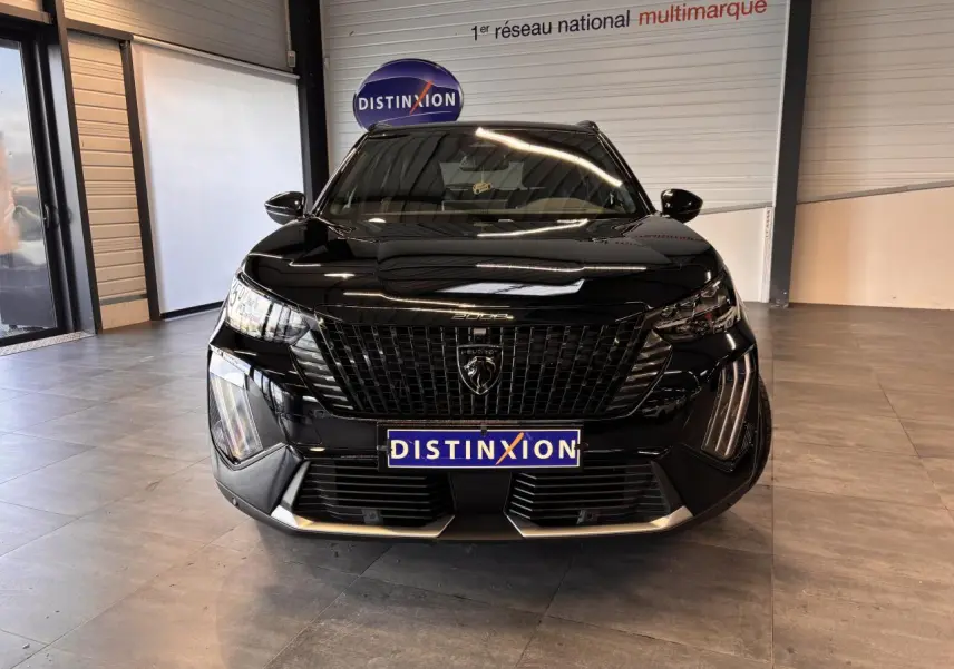 Vue frontale d’un Peugeot 2008 noir brillant avec calandre noire et feux LED en showroom.