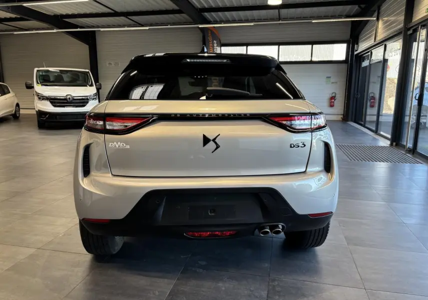 Vue arrière d'un DS3 Crossback 2024 Crystal Pearl avec double sortie d'échappement, en intérieur de showroom.