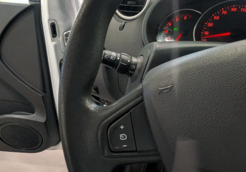 Vue rapprochée du volant et du tableau de bord du Renault Kangoo Express blanc, avec commandes au volant et compteurs rouges éclairés.