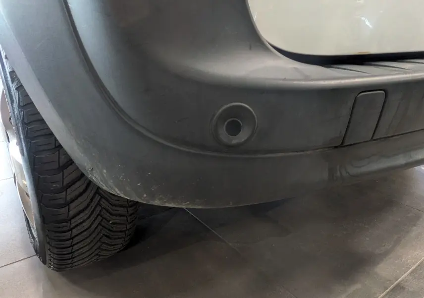 Gros plan sur le pare-chocs arrière droit blanc minéral du Renault Kangoo Express 2020 avec capteur de recul intégré.