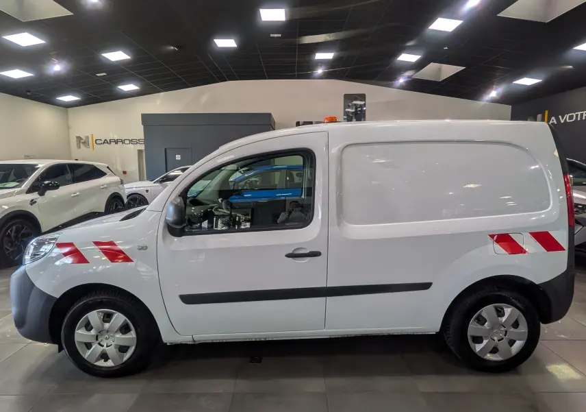 Vue de profil côté gauche d’un Renault Kangoo Express blanc minéral avec bandes réfléchissantes rouges sur ailes avant et arrière.