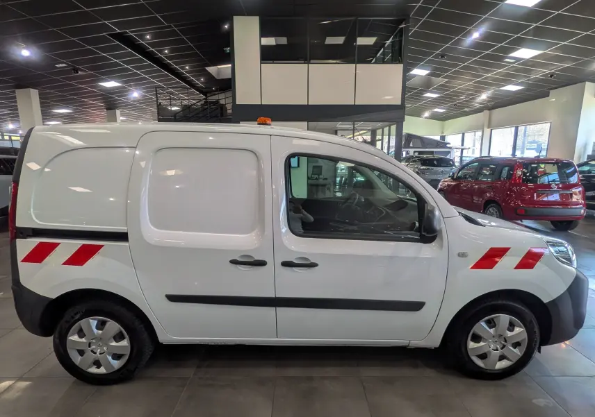 Vue de profil côté droit d’un Renault Kangoo Express blanc minéral avec bandes rouges réfléchissantes et gyrophare orange sur le toit.
