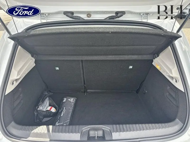Coffre ouvert vu de l'arrière d'une Renault Clio blanche, montrant un espace de rangement noir avec trousse de secours.
