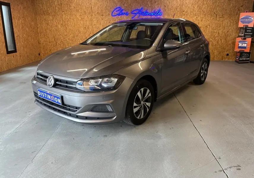 Volkswagen Polo 1.0 TSI gris vue 3/4 avant droit dans un showroom avec éclairage intérieur et logo néon bleu.