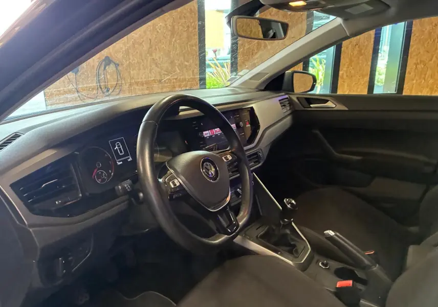 Vue intérieure côté conducteur d'une Volkswagen Polo 1.0 TSI 95 Confortline avec volant noir et boîte manuelle.