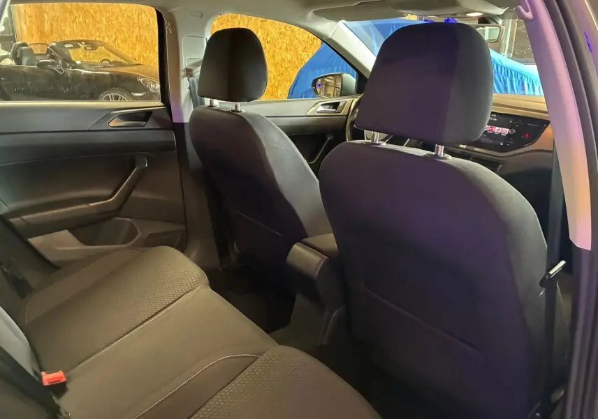 Vue intérieure arrière de la Volkswagen Polo gris 2018, montrant les sièges en tissu noir et le tableau de bord avant.