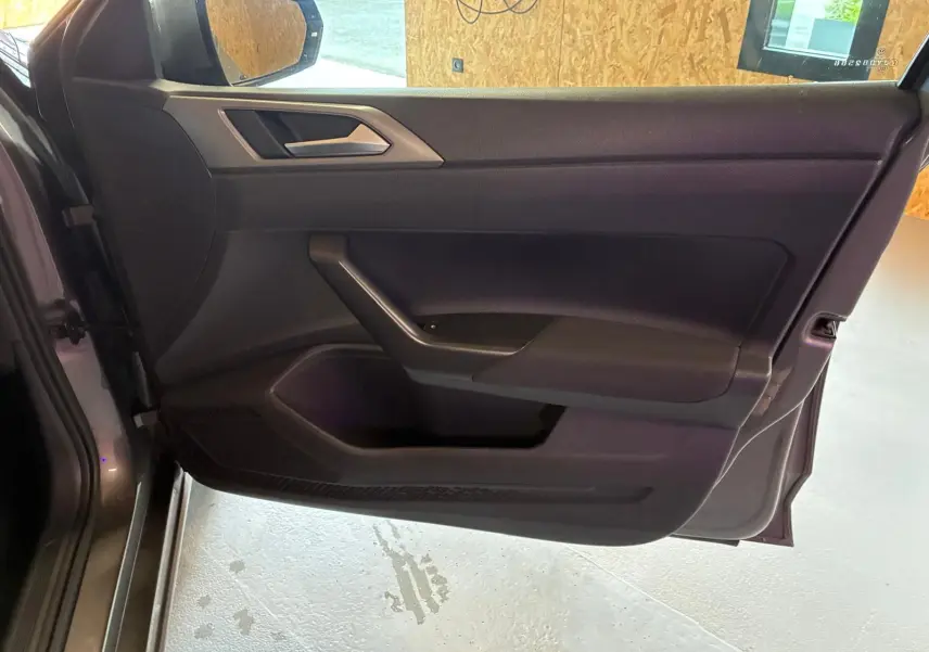 Vue intérieure de la porte avant gauche grise d'une Volkswagen Polo 2018, avec garniture noire et poignée intégrée.