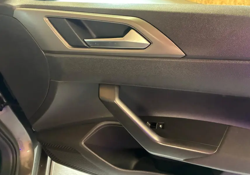 Vue rapprochée de la porte intérieure côté gauche d'une Volkswagen Polo gris foncé avec poignée argentée et commandes de fenêtre.