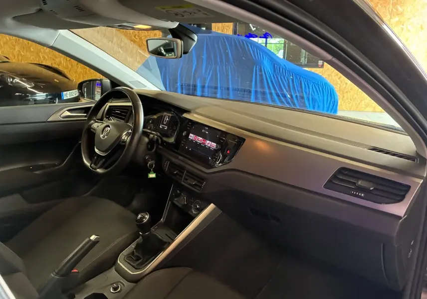 Vue intérieure côté conducteur de la Volkswagen Polo gris 2018, montrant le tableau de bord et la boîte manuelle.