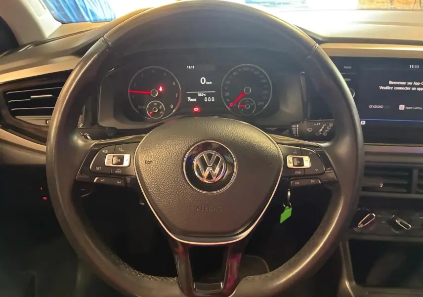 Vue centrée sur le volant noir de la Volkswagen Polo 2018 avec tableau de bord et écran multimédia en arrière-plan.