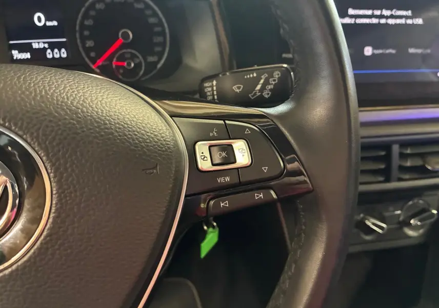 Gros plan sur le volant noir de la Volkswagen Polo 2018, avec commandes intégrées et tableau de bord numérique en arrière-plan.