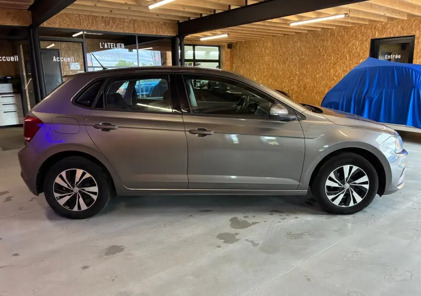 Vue de profil côté gauche d'une Volkswagen Polo gris métallisé 5 portes, stationnée dans un garage avec sol béton.