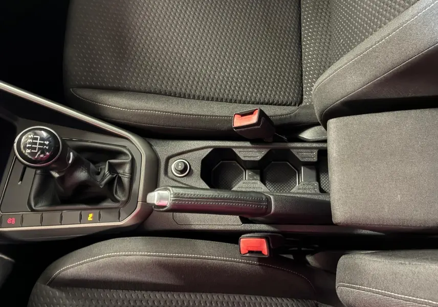 Vue rapprochée de la console centrale d’une Volkswagen Polo gris, montrant levier de vitesse manuel, frein à main et sièges en tissu noir.