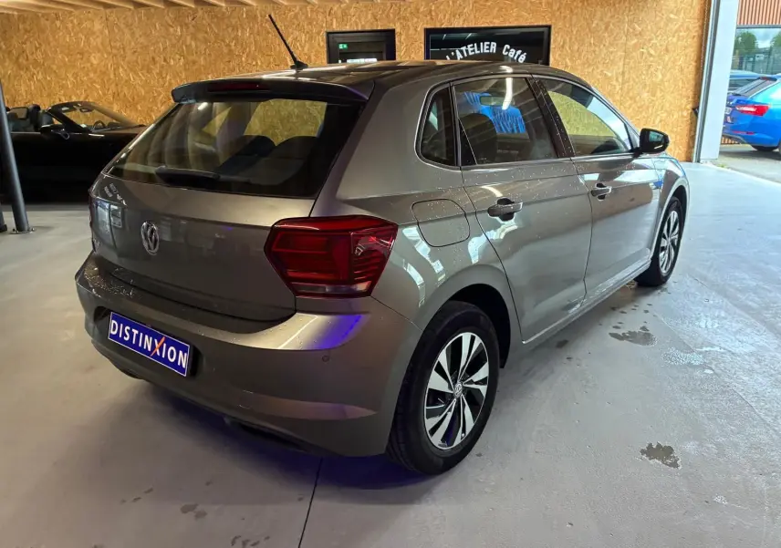 Volkswagen Polo gris vue 3/4 arrière droit dans un garage, avec jantes alliage et cinq portes visibles.