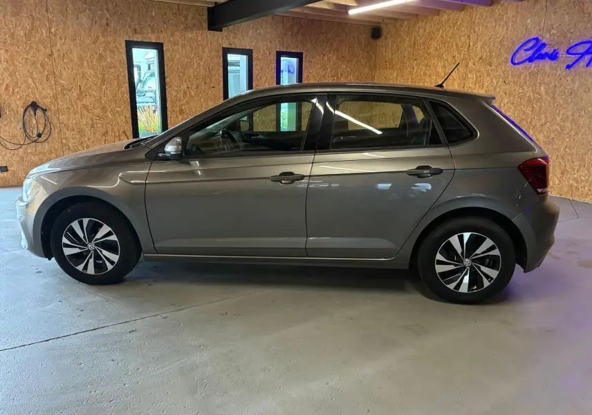Vue de profil côté gauche d'une Volkswagen Polo gris métallisé 5 portes, avec jantes noires et argentées, en intérieur.